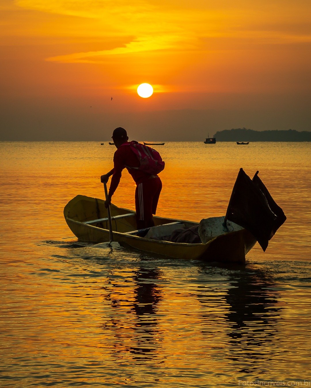Silhueta de uma pessoa remando um pequeno barco em águas calmas ao pôr do sol, com o sol junto ao horizonte e o céu em tons alaranjados.