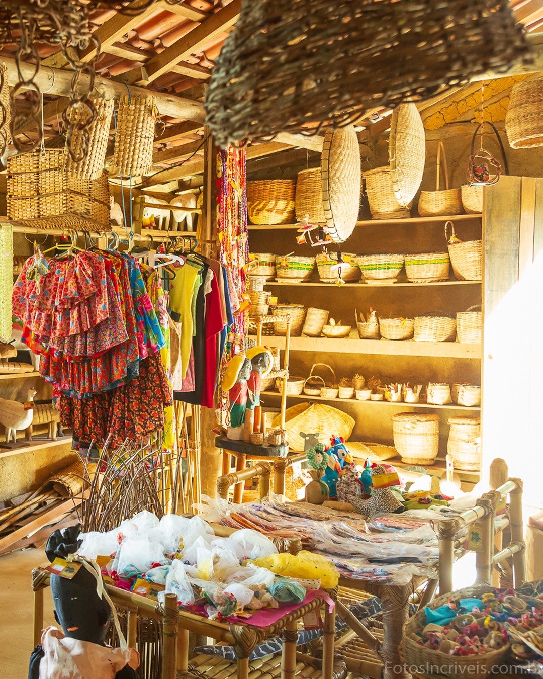 Interior de uma loja de artesanato rústica, com cestos de palha pendurados no teto, tecidos coloridos e prateleiras repletas de peças trançadas e cerâmicas.